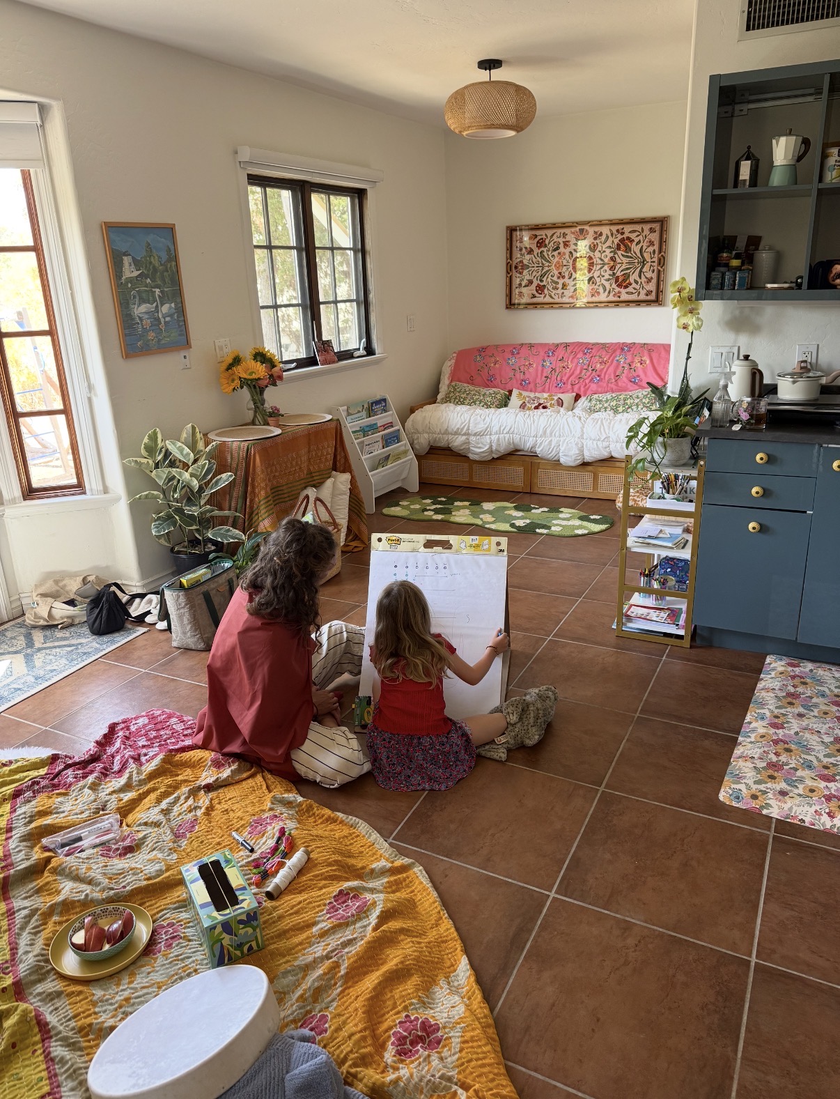 A bright enrichment room filled with books, plants and sunflowers as children work on the floor